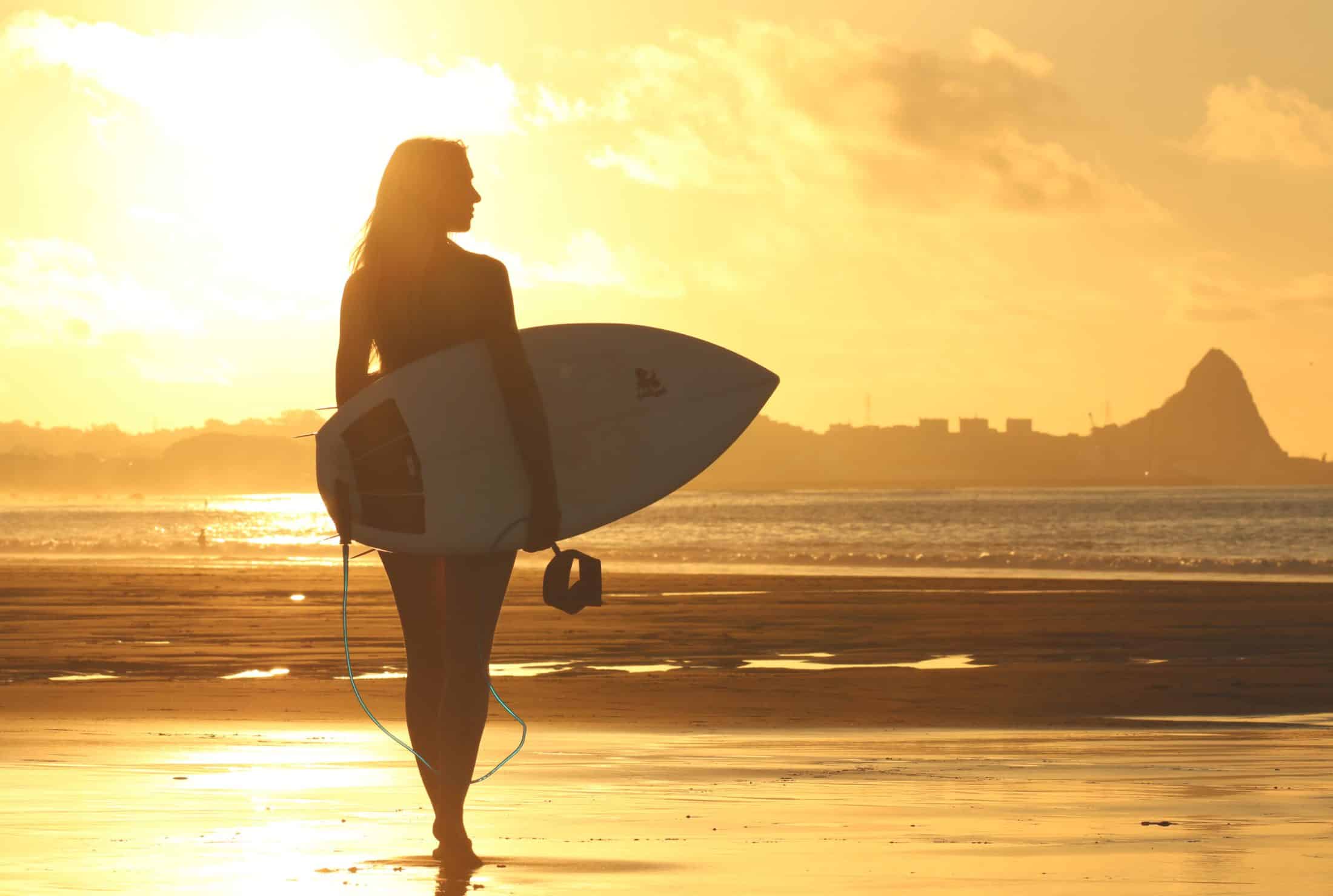 Silhouette of surfer girl with surfboard on beach at sunset. Witch's Rock Surf Camp.